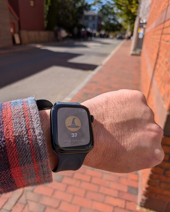 A WitchCatcher player's Apple Watch on a Salem brick sidewalk, showing 37 witch hats today